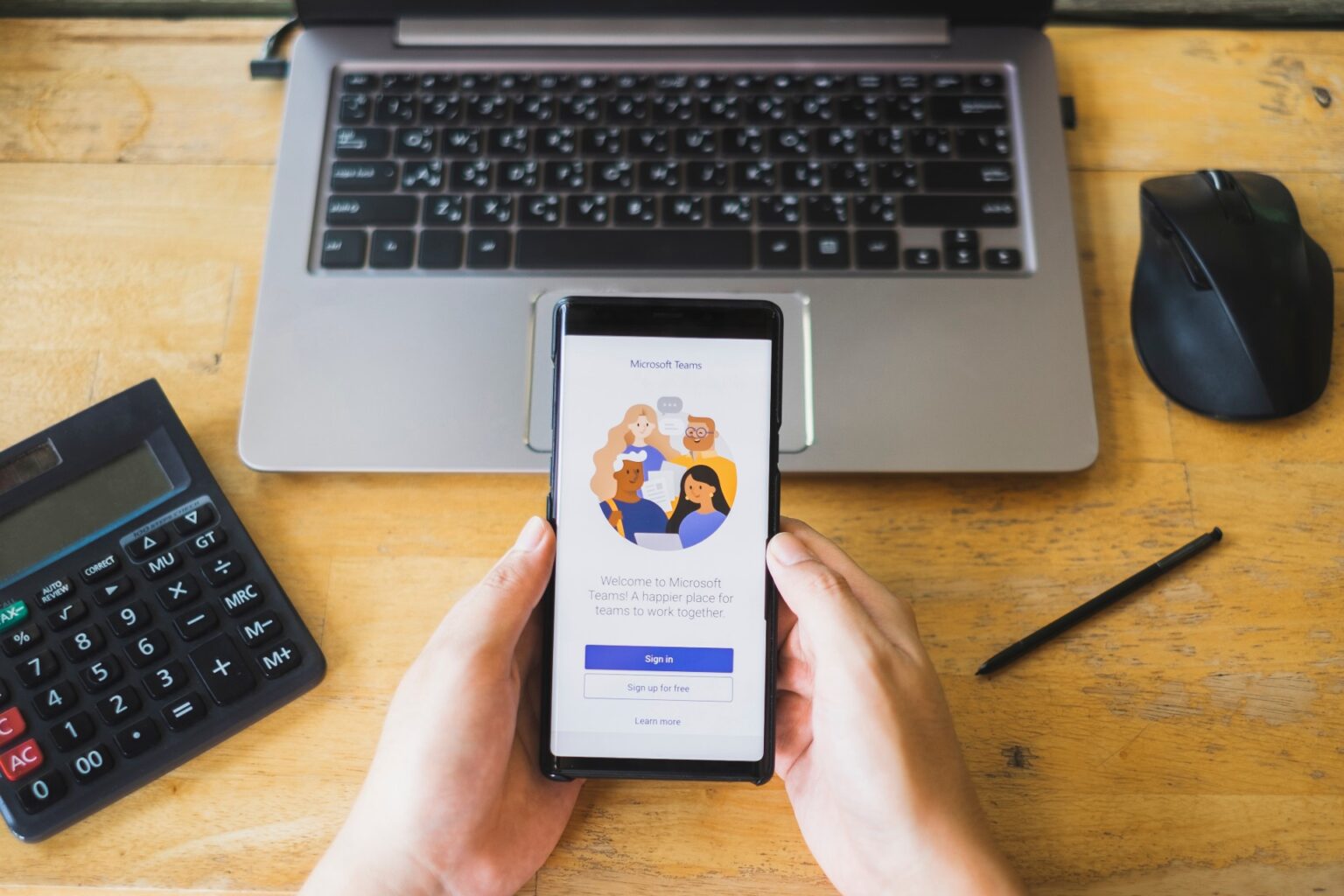A person using Microsoft Teams on a phone beside a laptop
